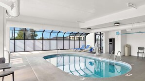 An indoor swimming pool with clear glass walls, blue lounge chairs, and a concrete floor. - Best Western Knoxville Suites - Downtown (Knoxville)