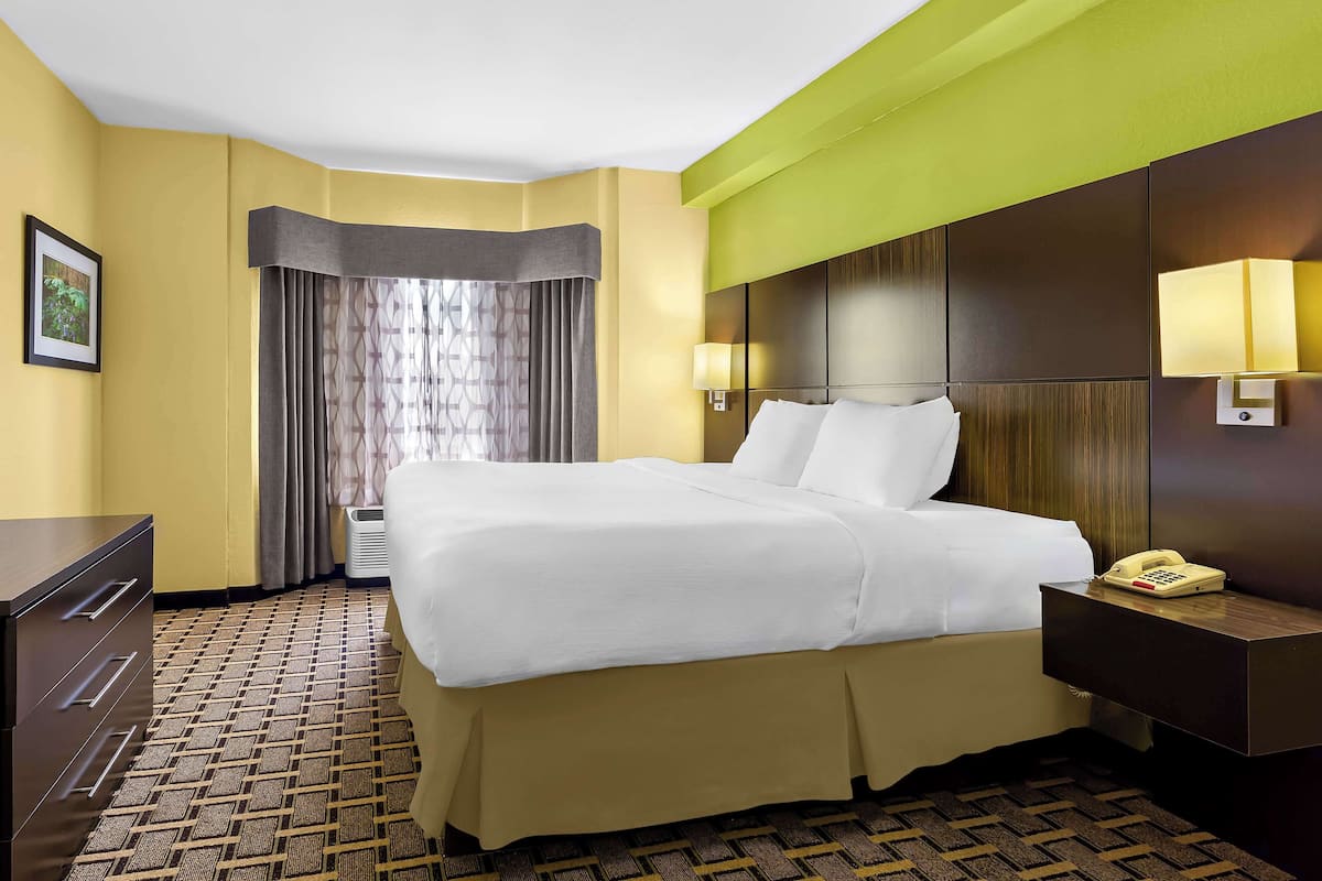 A hotel room with a neatly made bed, a bedside table with a lamp, a telephone, and a wall-mounted light.