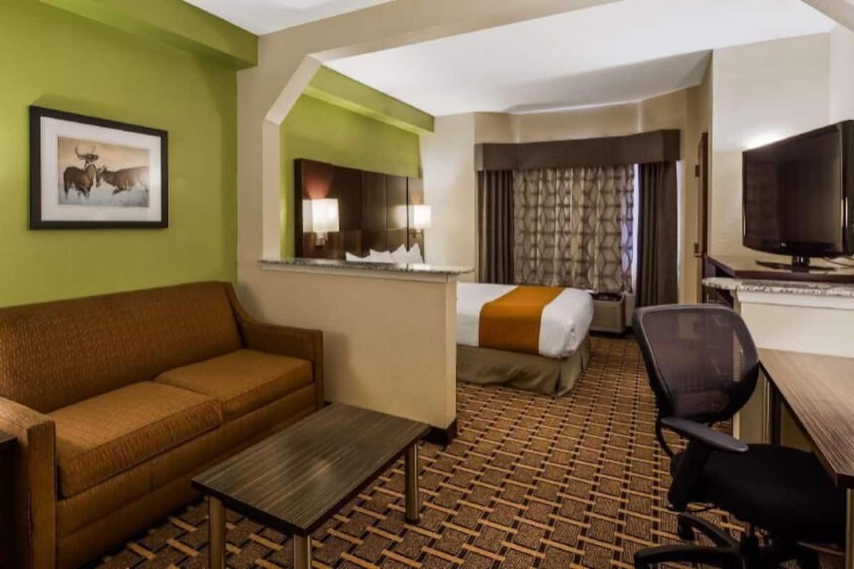 A hotel room with a sofa, a small table, a bed with a blanket, a TV, a desk, and a mirror.