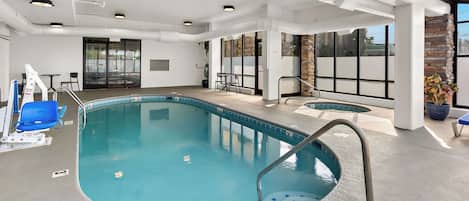 An indoor swimming pool with clear water, a lifeguard chair, and a poolside area with a table and chairs.