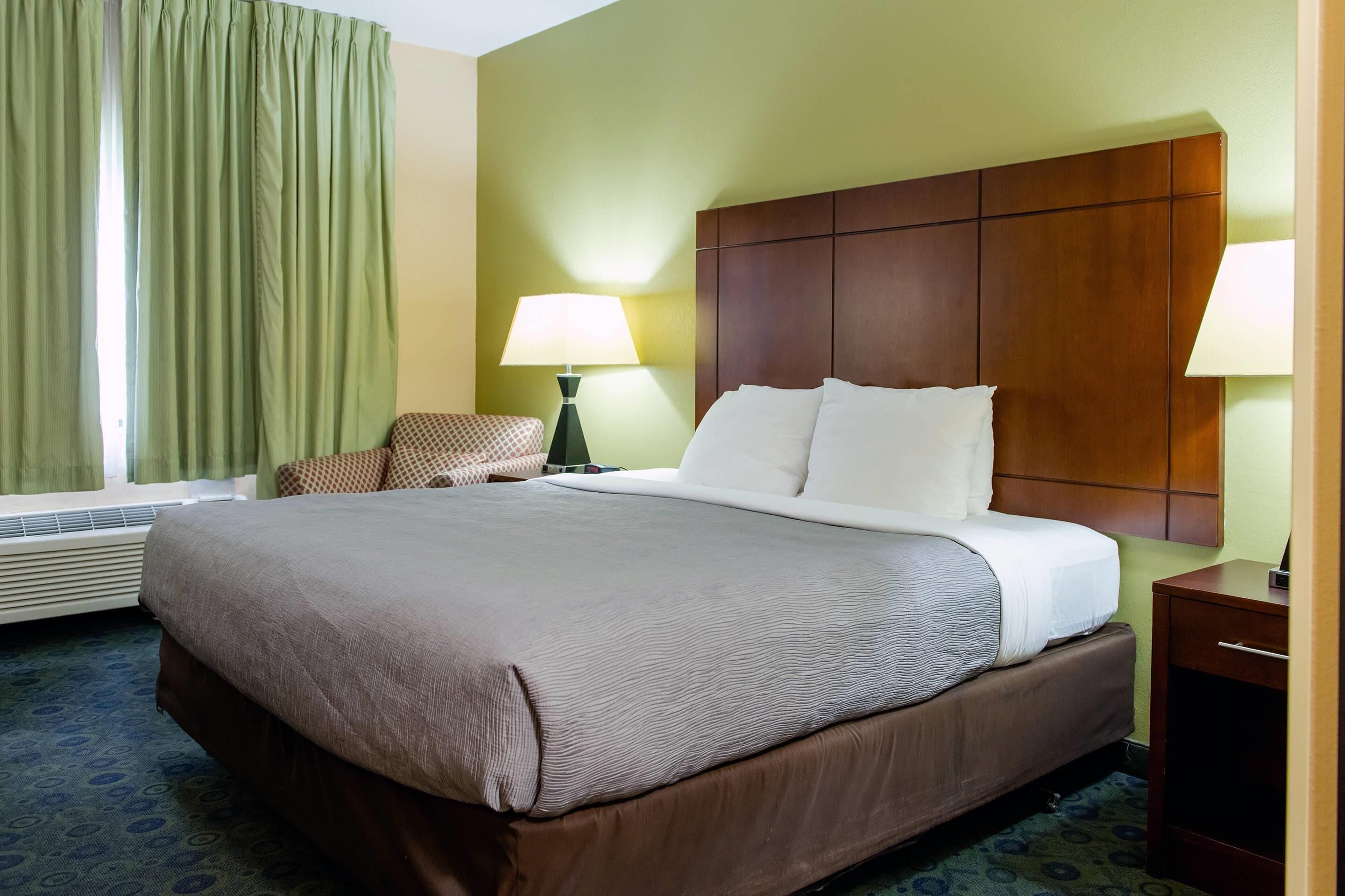 A hotel room with a large bed, two bedside lamps, a chair, and a wooden headboard.