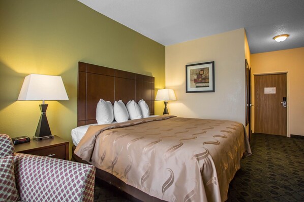 A hotel room with a large bed, two bedside lamps, a nightstand with a lamp, a chair, and a door. - Quality Inn & Suites Bloomington I-55 and I-74 (Bloomington)