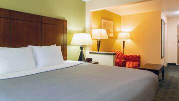 A hotel room with a large bed, two bedside lamps, a red armchair, a small table, and a nightstand.