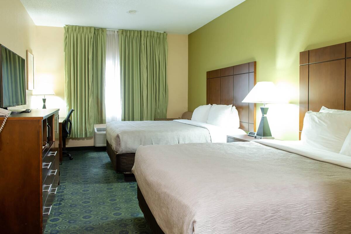 A hotel room with two beds, a desk, a chair, and a dresser.