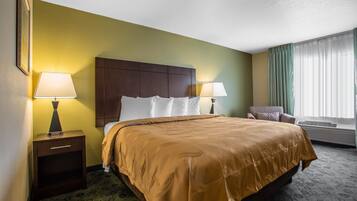 A hotel room with a large bed, two bedside lamps, a nightstand, a chair, and a window with curtains.