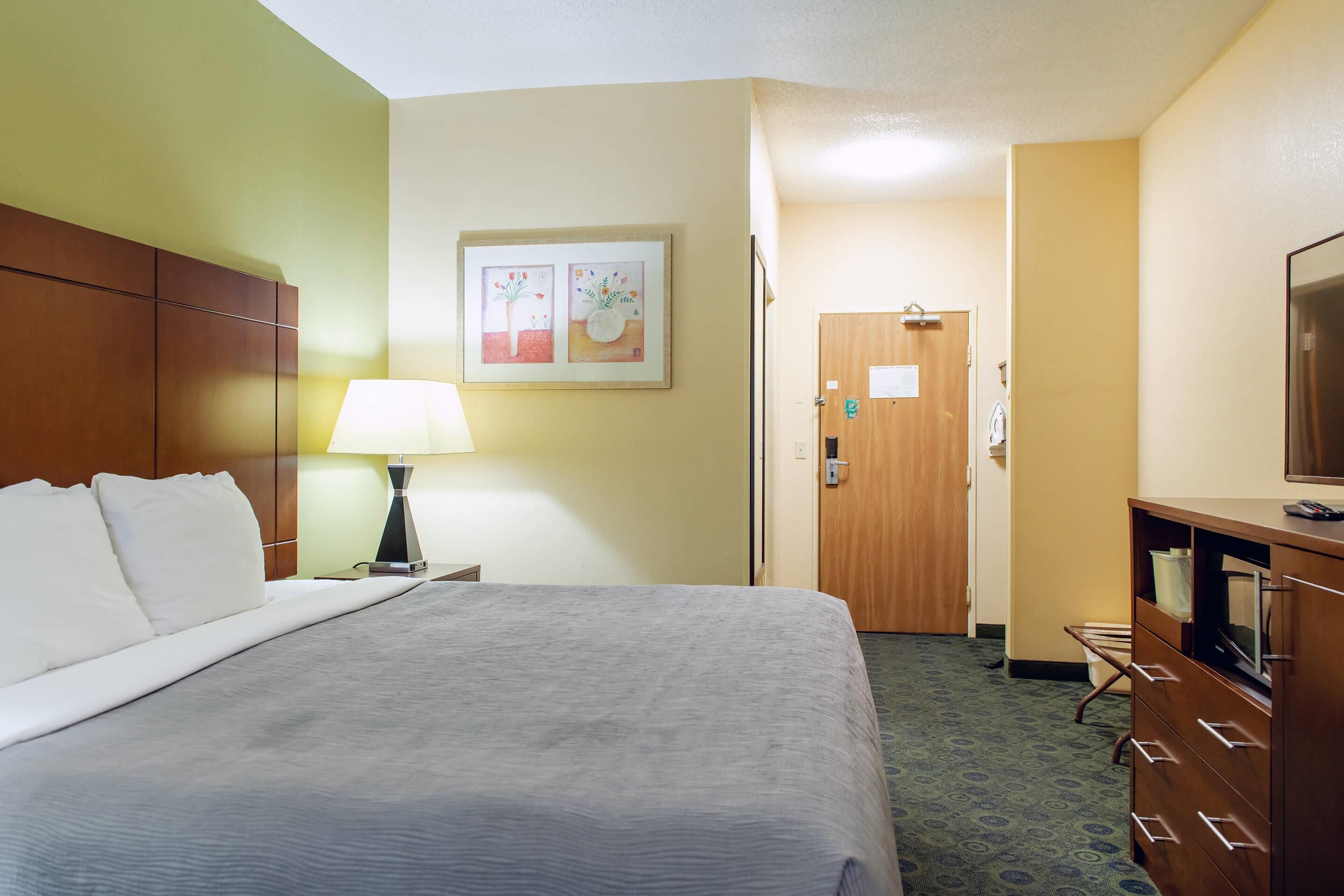 A hotel room with a bed, a desk, a lamp, a television, and a door.