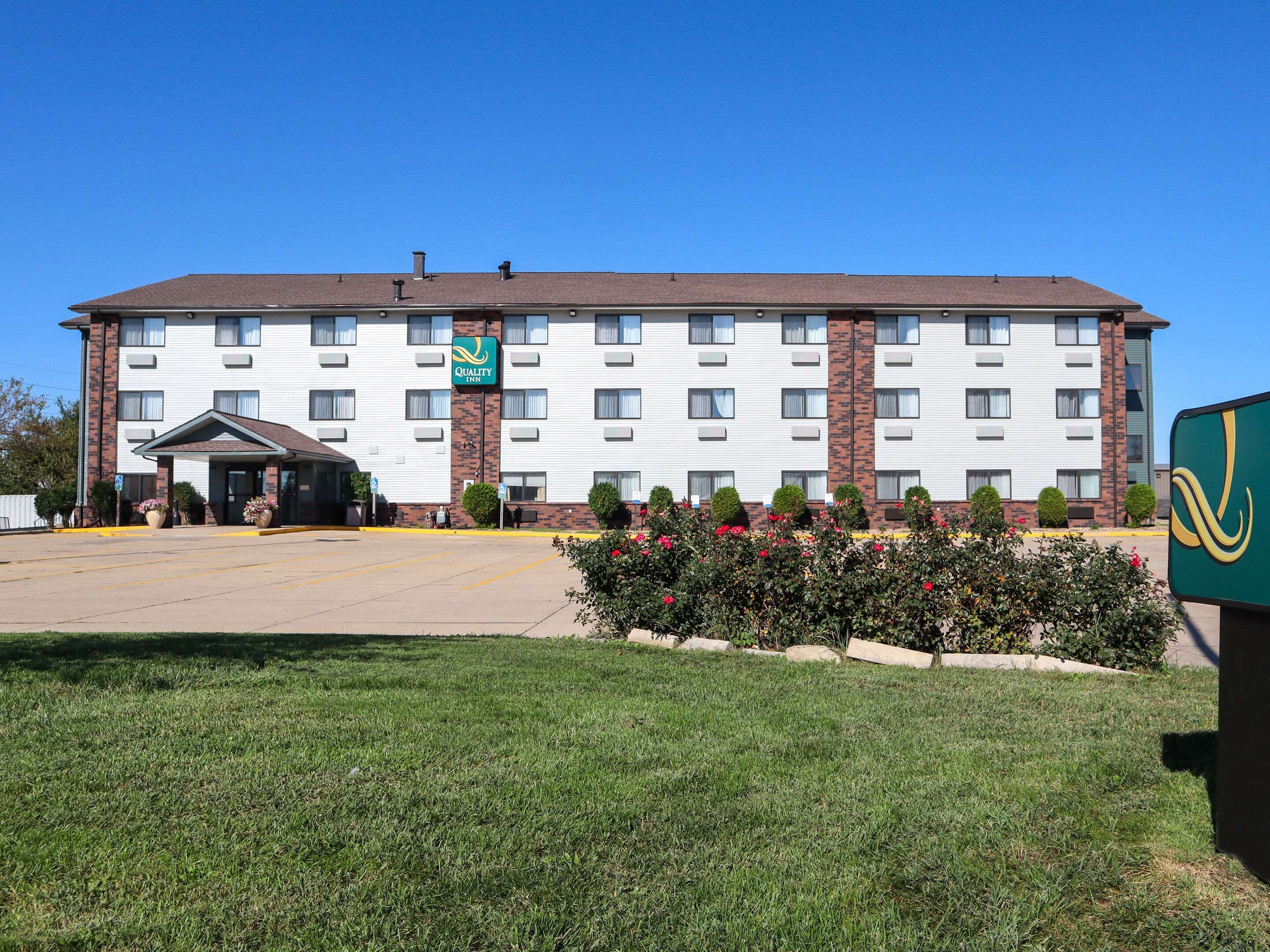 A multi-story hotel with a central entrance, a brick facade, and a parking lot in front.