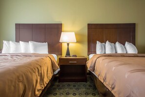 A hotel room with two beds, a nightstand with a lamp, and a digital clock.