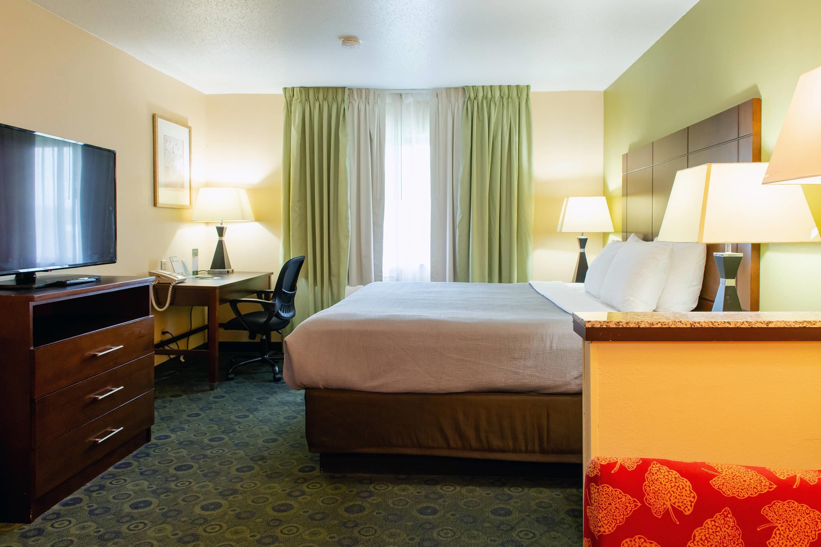 A hotel room with a bed, desk, chair, television, and lamps.