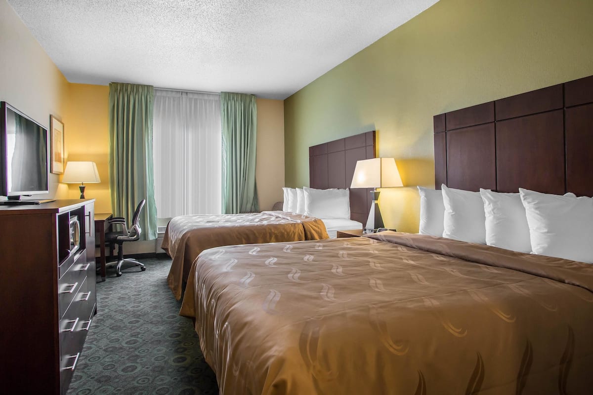 A hotel room with two beds, a desk, a TV, and a window with curtains.