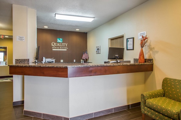 A hotel reception desk with a sign reading "Quality Inn & Suites by Choice Hotels," an American flag, and a "Manager on Duty" sign.