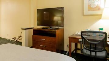 A hotel room with a bed, a desk with a computer, a TV on a wooden stand, and a chair.