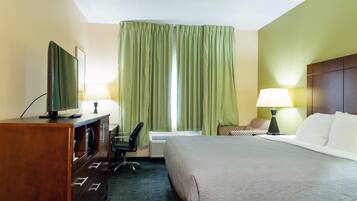 A hotel room with a bed, a desk with a TV, a chair, a lamp, and a window with curtains.