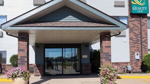 A hotel entrance with a covered entryway, large glass doors, and a brick pillar. - Quality Inn & Suites Bloomington I-55 and I-74 (Bloomington)
