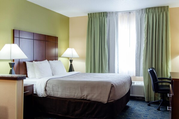 Una habitación de hotel con cama, dos lámparas de noche, un escritorio con silla y una ventana con cortinas.