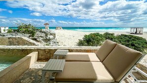 Un salón junto a la playa con piscina, una mesa y una zona de estar con cojines.