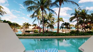 Relax by the resort pool surrounded by lush palm trees and a thatched-roof structure.