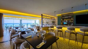 Un restaurante con mesas dispuestas para comer, una zona de bar con taburetes y una pared llena de botellas.
