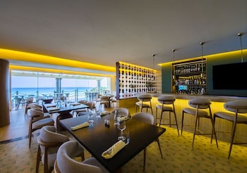 A beachside lounge with a pool, a table, and a cushioned seating area. at Grand Park Royal Cancun - All Inclusive
