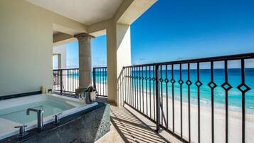 A balcony with a view of the ocean, a bathtub, and a pool.