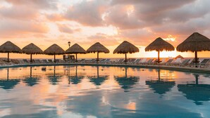 A poolside area with lounge chairs and thatched umbrellas, reflecting a sunset sky. - Grand Park Royal Cancun -  All Inclusive (Cancun)