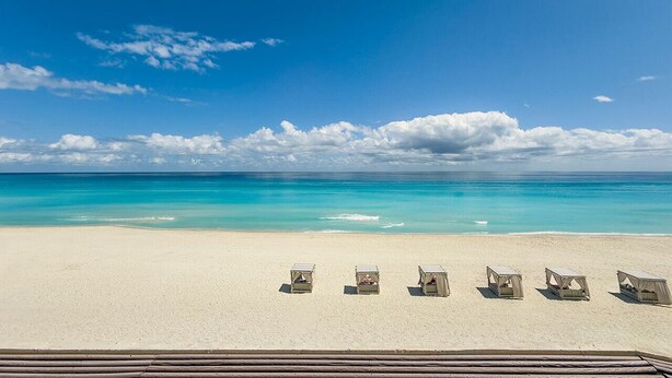 Una playa con cinco cabañas de playa alineadas, cielo azul despejado y océano turquesa.