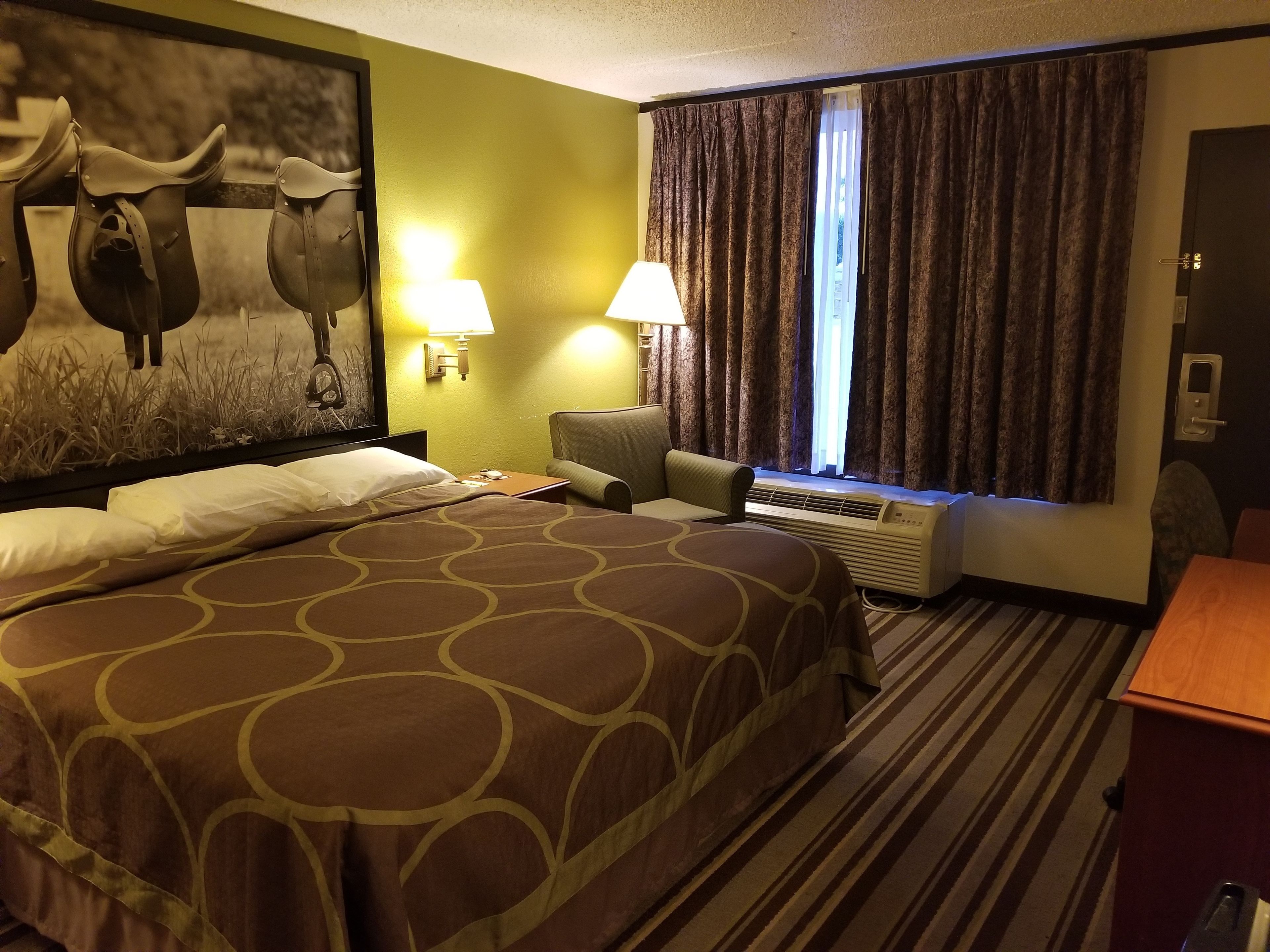 Ein Hotelzimmer mit einem großen Bett, zwei Nachttischlampen, einem Sessel, einem Schreibtisch und einem fenster mit Vorhängen.