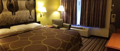 Ein Hotelzimmer mit einem großen Bett, zwei Nachttischlampen, einem Sessel, einem Schreibtisch und einem fenster mit Vorhängen.