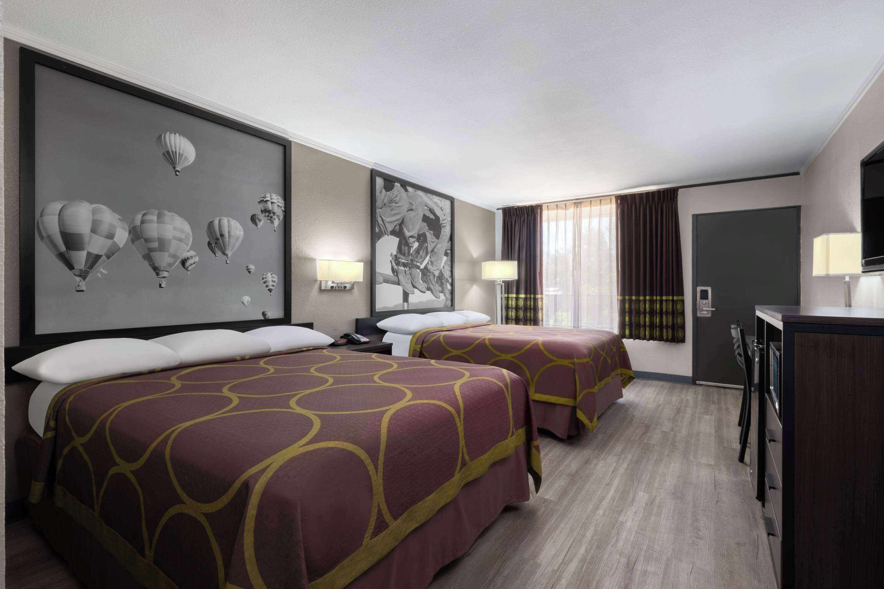 A hotel room with two beds, a desk, a TV, and a large framed picture of hot air balloons on the wall.