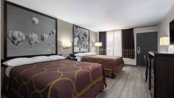 A hotel room with two beds, a desk, a TV, and a large framed picture of hot air balloons on the wall.