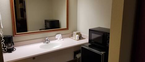 Un baño de hotel con lavamanos, espejo, cafetera y microondas.