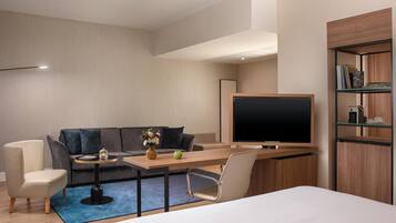 Una habitación de hotel moderna con sofá, una mesita con un florero y una manzana, televisión y estantería.