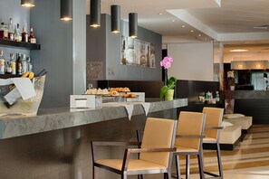 A modern bar area with a marble countertop, bar stools, and a variety of bottles and snacks.