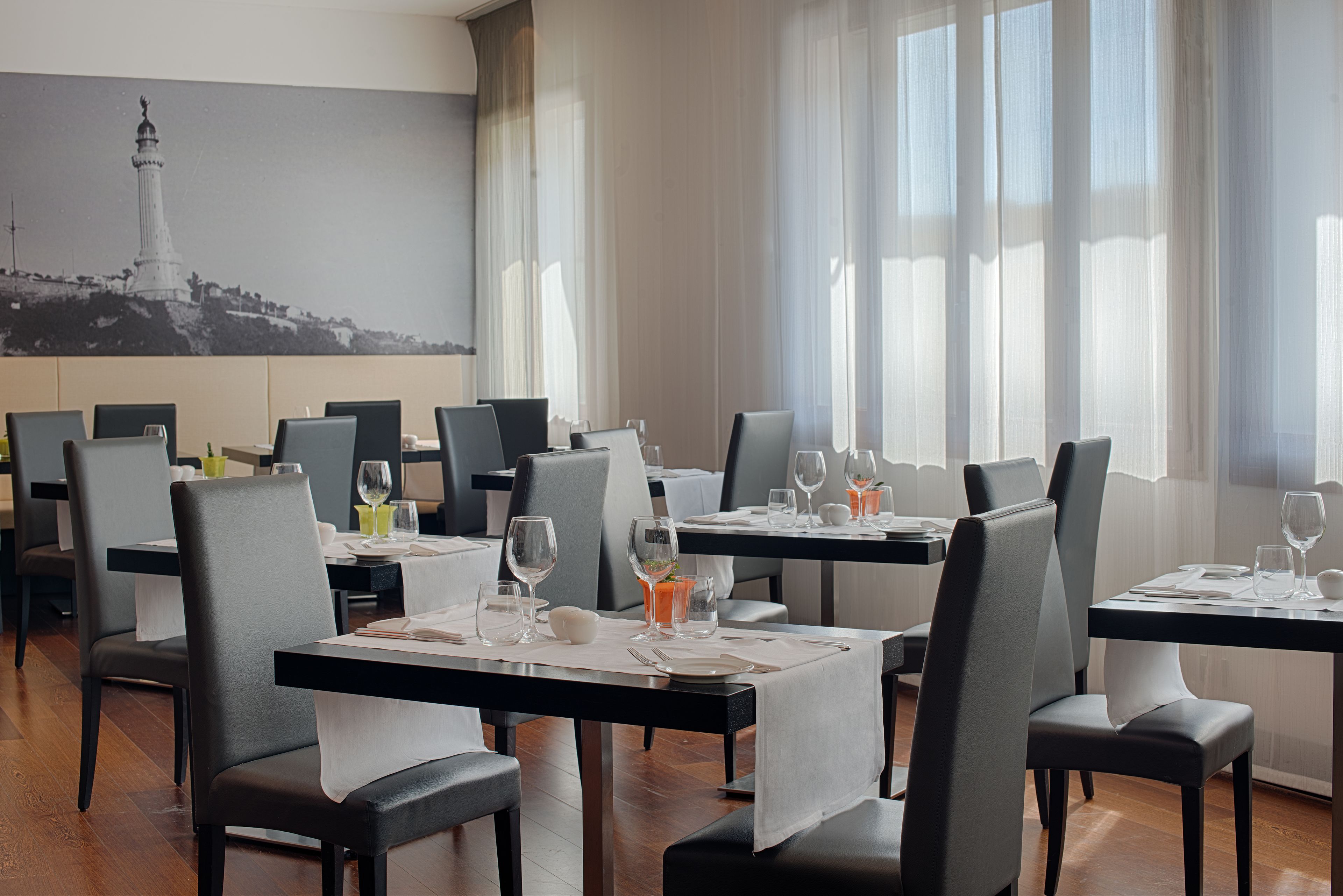 A restaurant with tables set for dining, chairs, and a large painting of a lighthouse on the wall.