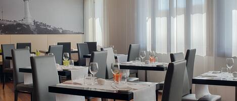 A restaurant with tables set for dining, chairs, and a large painting of a lighthouse on the wall.
