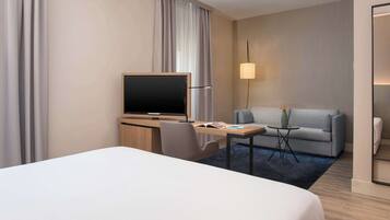 Una habitación de hotel con cama, escritorio con televisor, sofá y lámpara.