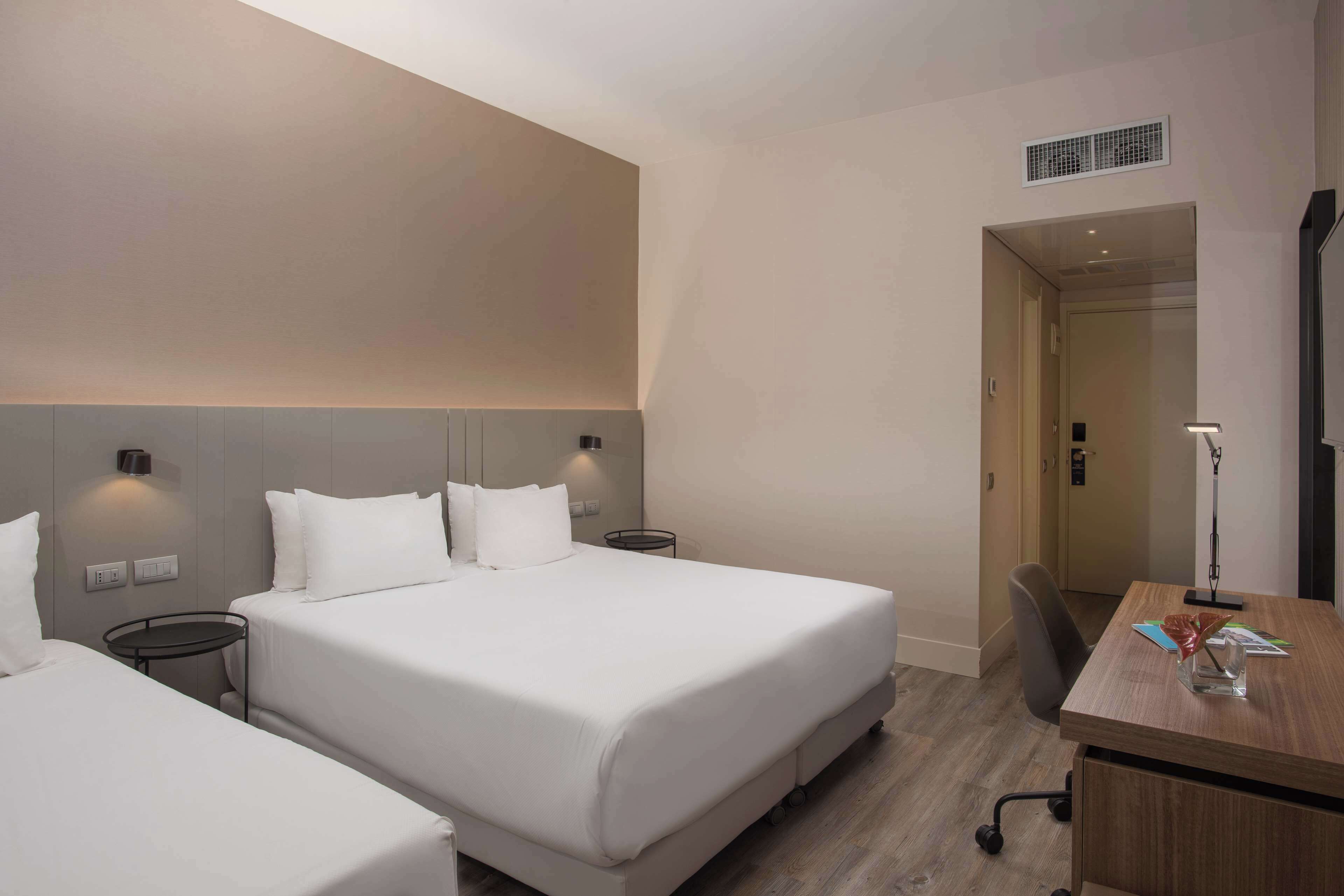 A hotel room with two beds, a desk, and a chair.