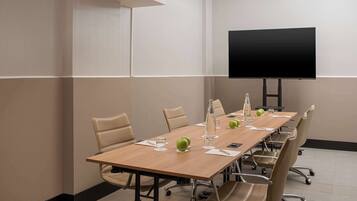 Une salle de conférence avec une longue table, des chaises, un téléviseur à écran plat et une bouteille d’eau.