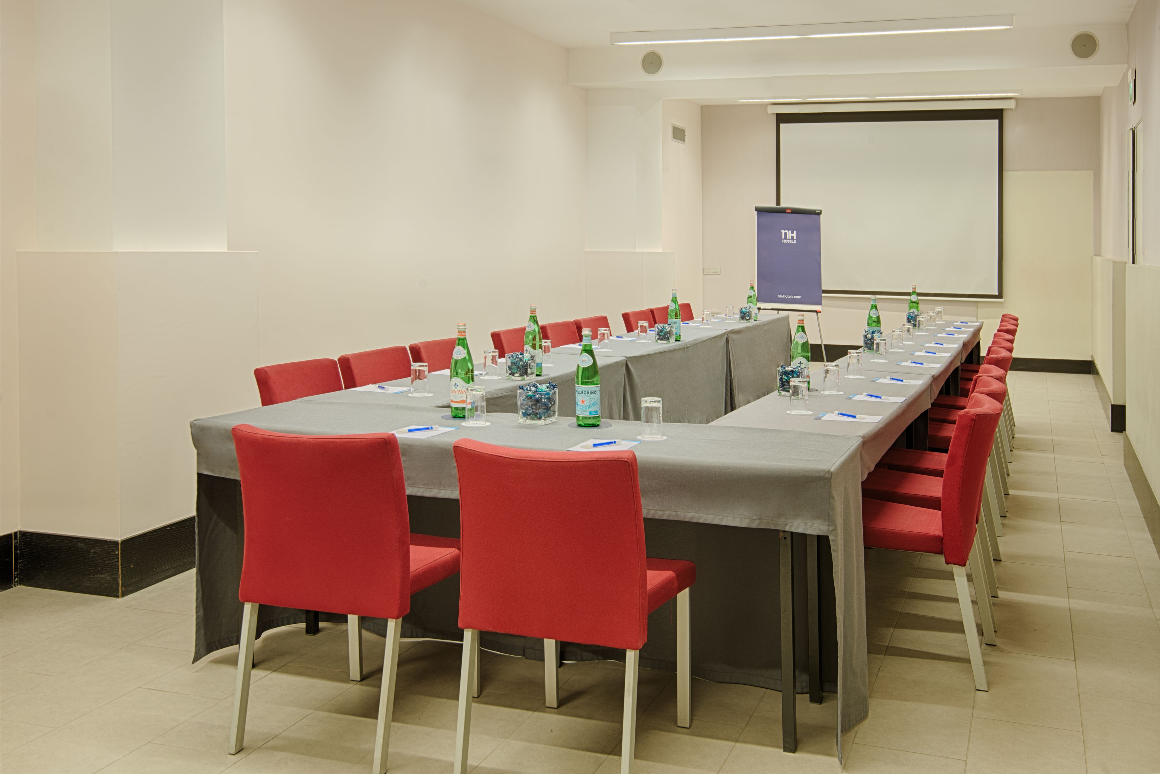 A conference room with a long table, red chairs, and a projector screen.