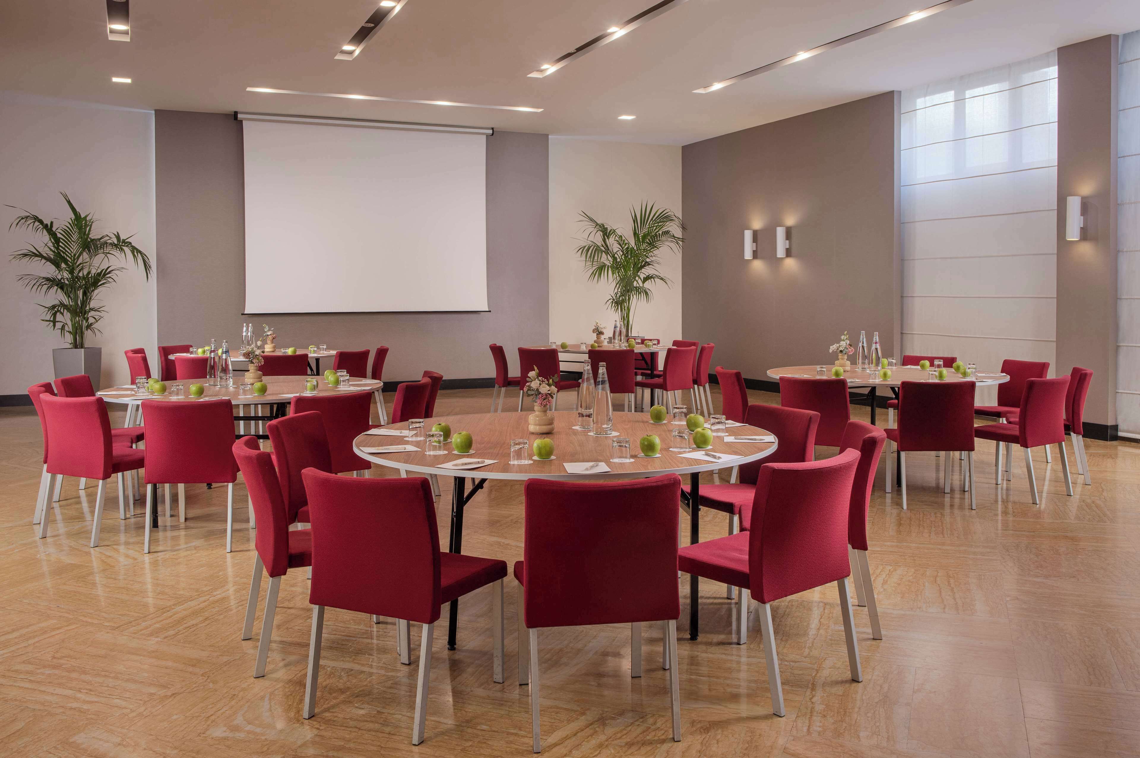 A conference room with round tables, red chairs, and a projector screen.