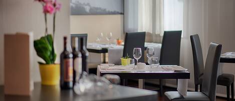 Un comedor con una mesa lista para dos personas, una planta en maceta y una botella de vino.