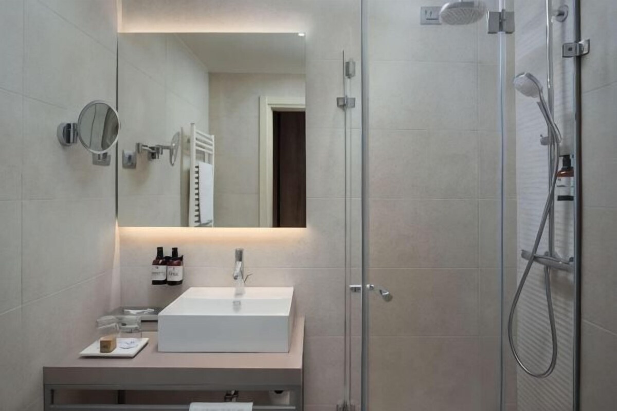 A modern bathroom with a white sink, a mirror, a handheld showerhead, and a glass shower enclosure.