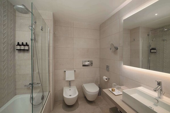 A modern bathroom with a glass-enclosed shower, a bidet, a toilet, and a large mirror above a sink.