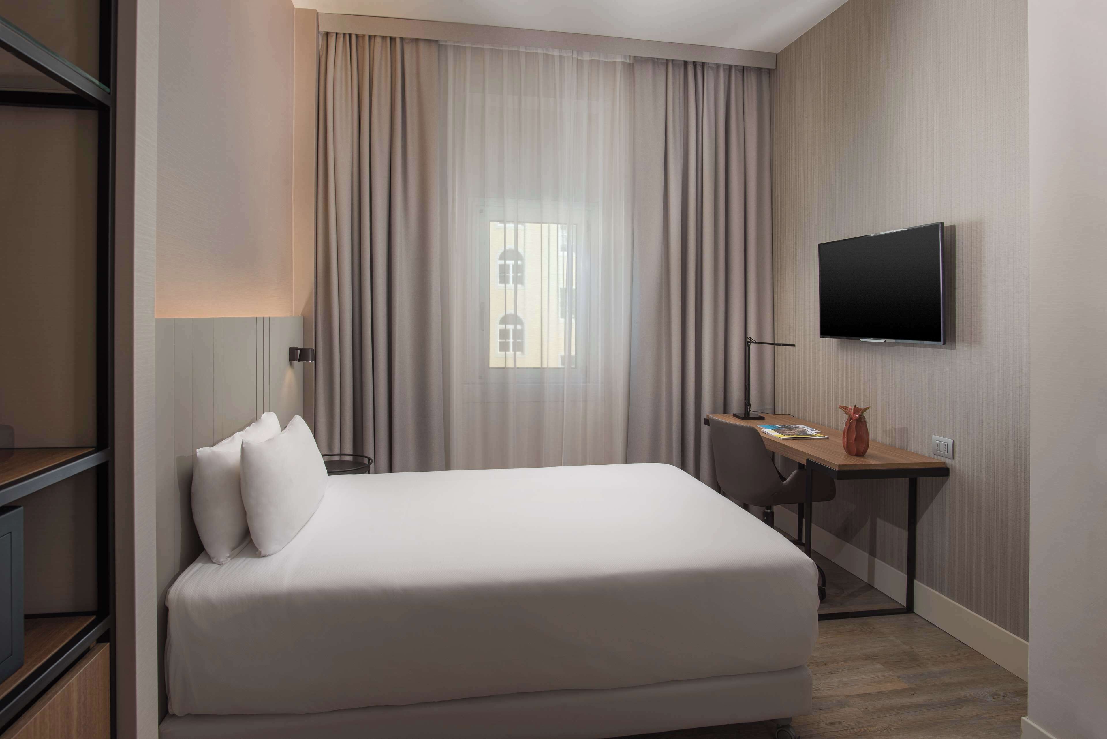 Een hotelkamer met een bed, bureau, televisie en raam met gordijnen.