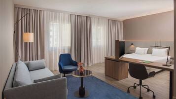 A hotel room with a sofa, a chair, a desk, a bed, and a TV.