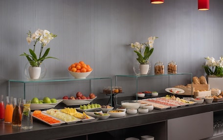 A buffet with various food items, including fruits, vegetables, and meats, arranged on a glass display.