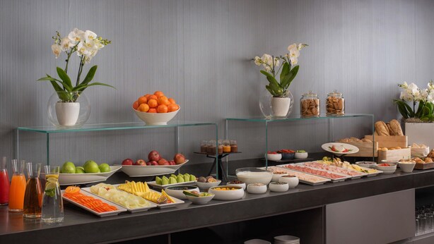 A buffet with various food items, including fruits, vegetables, and meats, arranged on a glass display. - NH Trieste (Trieste)