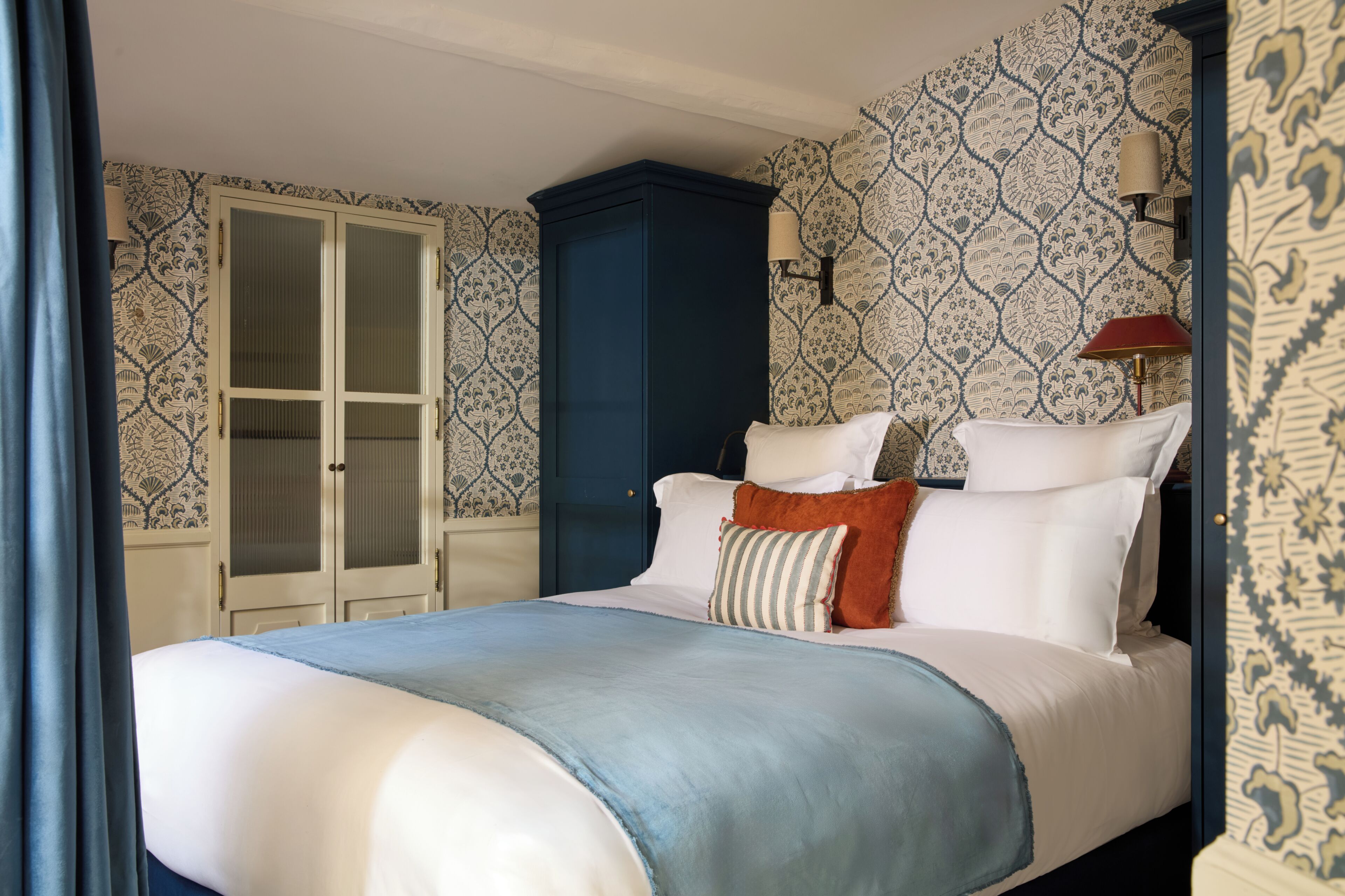 A bedroom with a bed, a wardrobe, and patterned wallpaper.