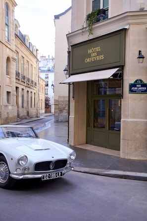 A classic white convertible parked in front of a hotel named 'Hôtel des Orfèvres' with a sign indicating 'RUE JEAN LANTIER.'