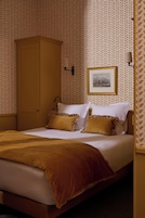 Una habitación de hotel con una cama, un armario, un cuadro en la pared y un papel tapiz estampado.